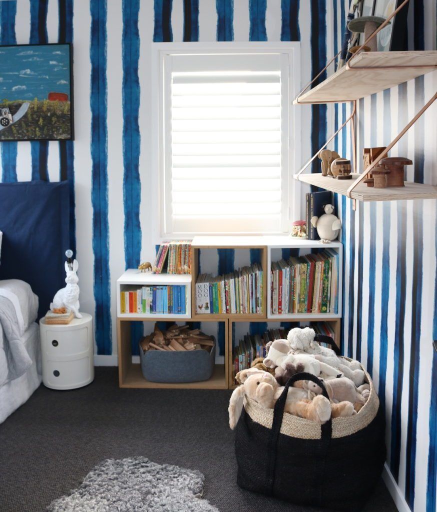 Boys bedroom with Shibori Stripe Wallpaper hung vertically with a basket of stuffed animals and a bookshelf full of childrens' books.