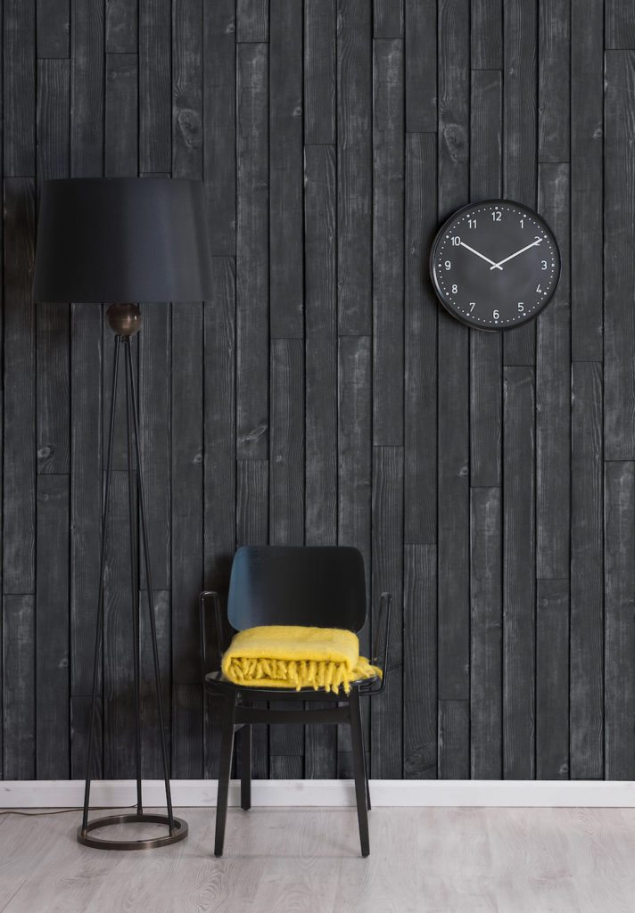 Black Wooden Boards Wallpaper. Wallpaper with black faux timber look with black lamp shade, black lamp stand, black wall clock and black chair and yellow blanket