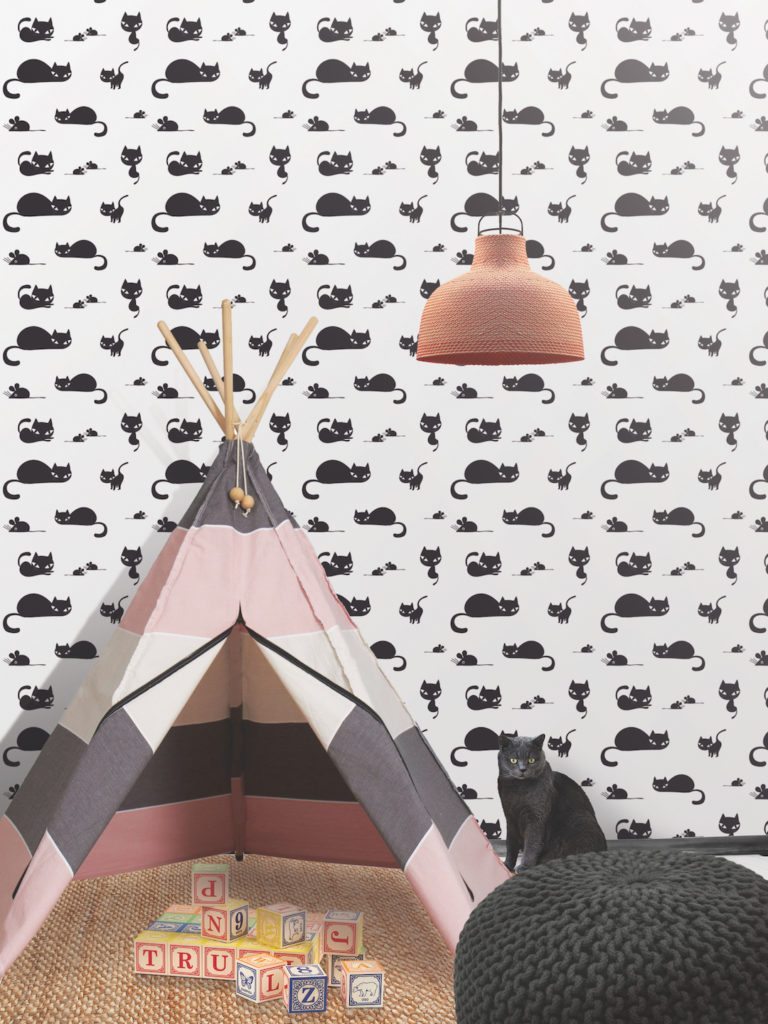 White Wallpaper with Black Cats called Meow from Milton & King. In front of the wallpaper is a striped tent, letter blocks on the ground a black crochet stool and a black cat. 