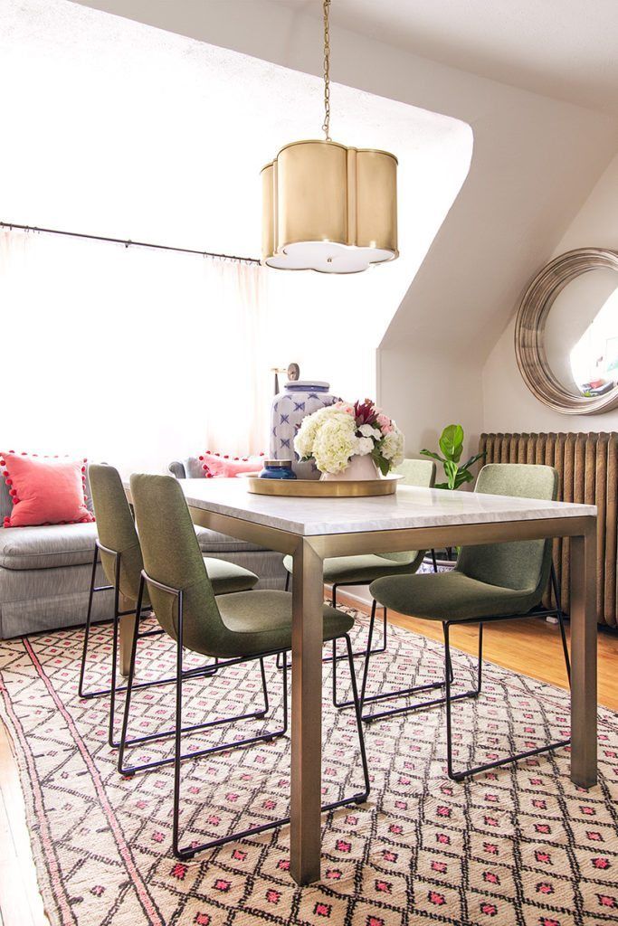 A dining table with marble top and brass frame and legs. Four olive green mid-century modern style chairs are around the table with a brass pendent lamp hanging from the ceiling. The table sits on top of Moroccan wool rug