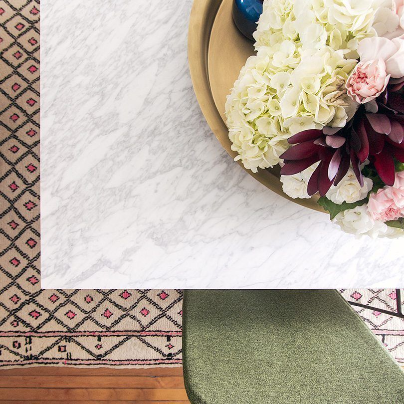 close up overhead photo of the edge of the marble topped dining table. In the center is an arrangement of florals with pink, white and red flowers.
