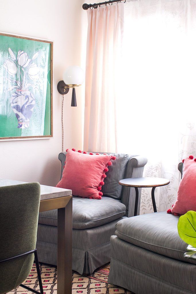 two vintage gray slip chairs with salmon colour pillows with a picture on the left wall of a blue and white vase with flowers against a green background