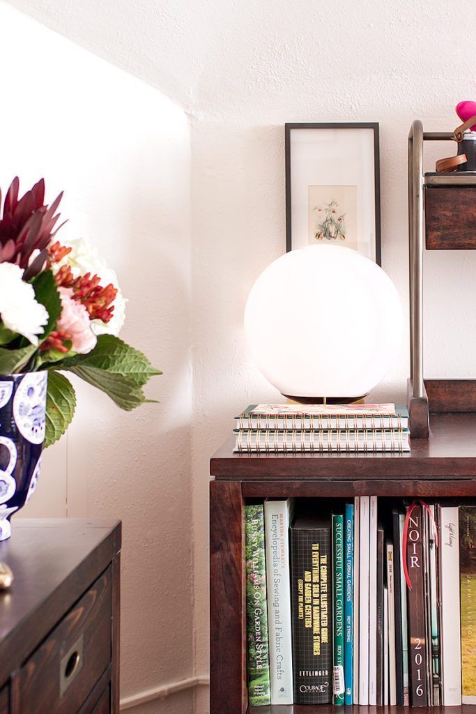 pictured is a storage unit made of modular craft room furniture with trade catalogs, wallpaper samples, and other items. On top of the furniture is a round lightbulb lamp.