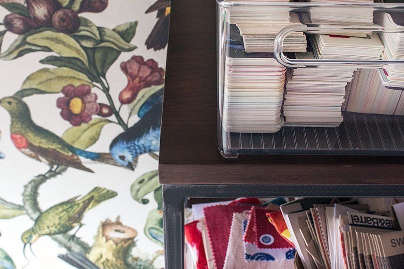 a close up of the walnut shelving with fabric samples, wallpaper samples and the Orinthology Wallpaper by Milton & King in the background. 