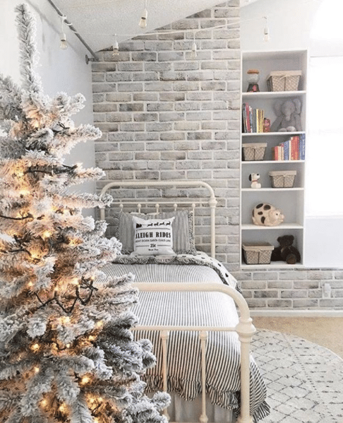 girl's bedroom with limewashed brick wallpaper behind the bed and a frost covered fake tree at the foot of the bed.