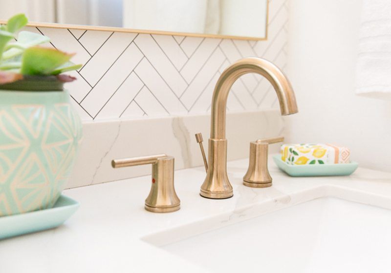 Close up photo of the brass plated faucets in the bathroom with Tile Progress Wallpaper from Milton & King in the background