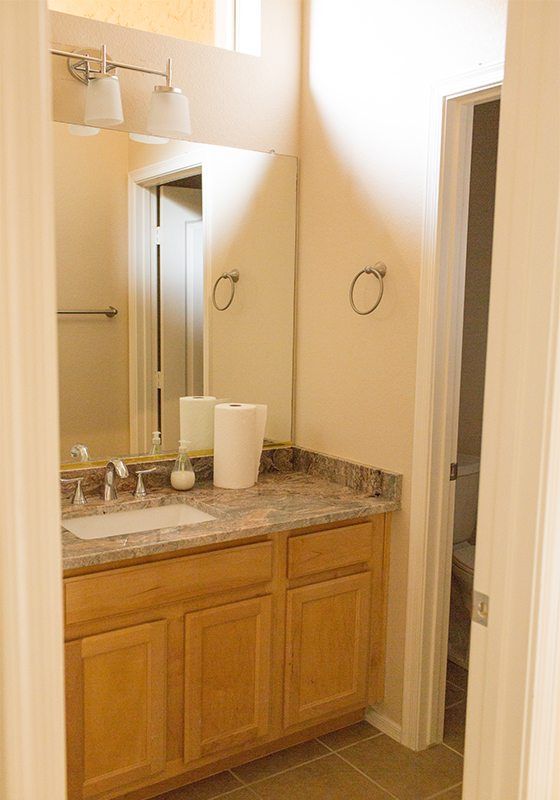 before the guest bathroom remodel photo showing light wood vanity with bare walls and beige marbled counter top