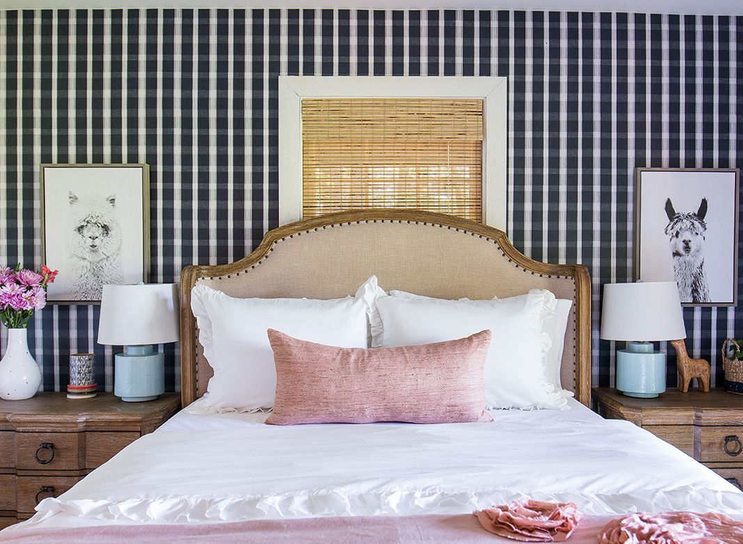 Bedroom with Bedroom wallpaper in a plaid pattern called monarch from Milton & King. A Queen sized bed with white and pink linen. Two bedside tables with pink flowers on the left and two black and white photos of llamas above each bedside table.