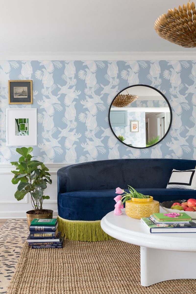 Jewel Marlow Basement Makeover • There is a leopard area rug a white round coffee table, a blue sofa and Magpie Wallaper from Mliton and King on the back wall with a big circular mirror mounted on the wall