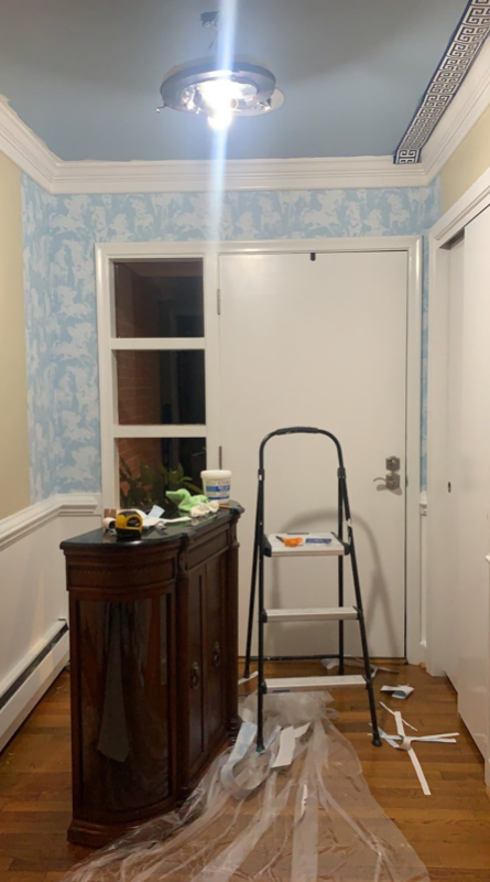 installing light blue wallpaper. there is plastic on the floor to protect it from any glue that might drip