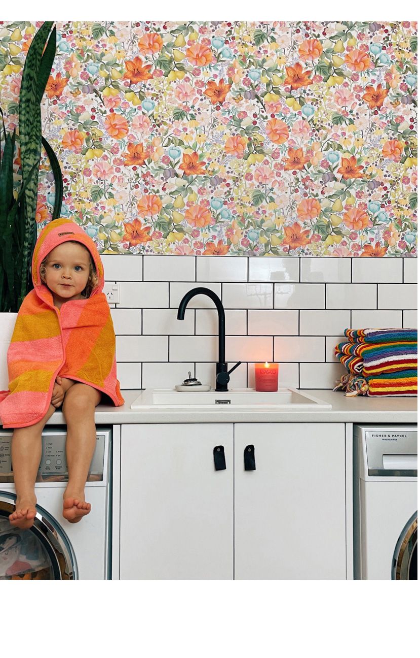 Abundance Wallpaper • Kip&Co • Colorful Floral Wallpaper • laundry room insitu with young girl sitting on washing machine by Rosie Clark