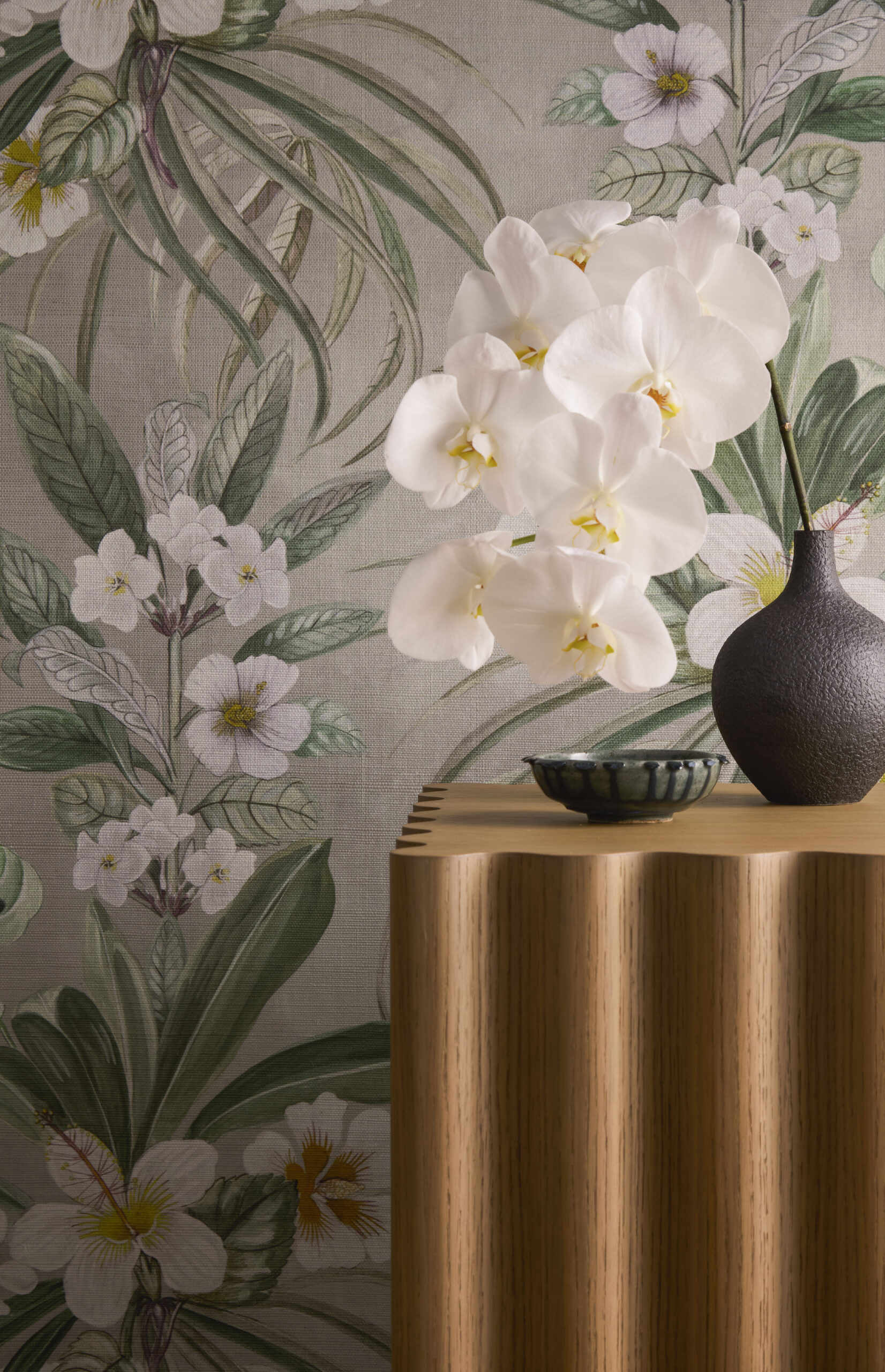 Hibiscus at Double Bay Grasscloth Wallpaper in front of a small table stand with a vase that has some hibiscus flowers in it.