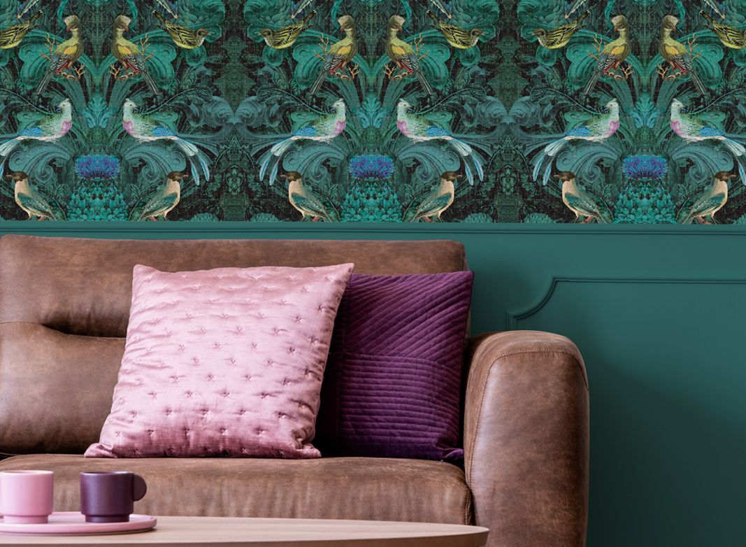 Flamboyant Wallpaper called Birdlife with a brown leather couch two purple cushions. In front of the couch is a brown round table with two purple candles on it