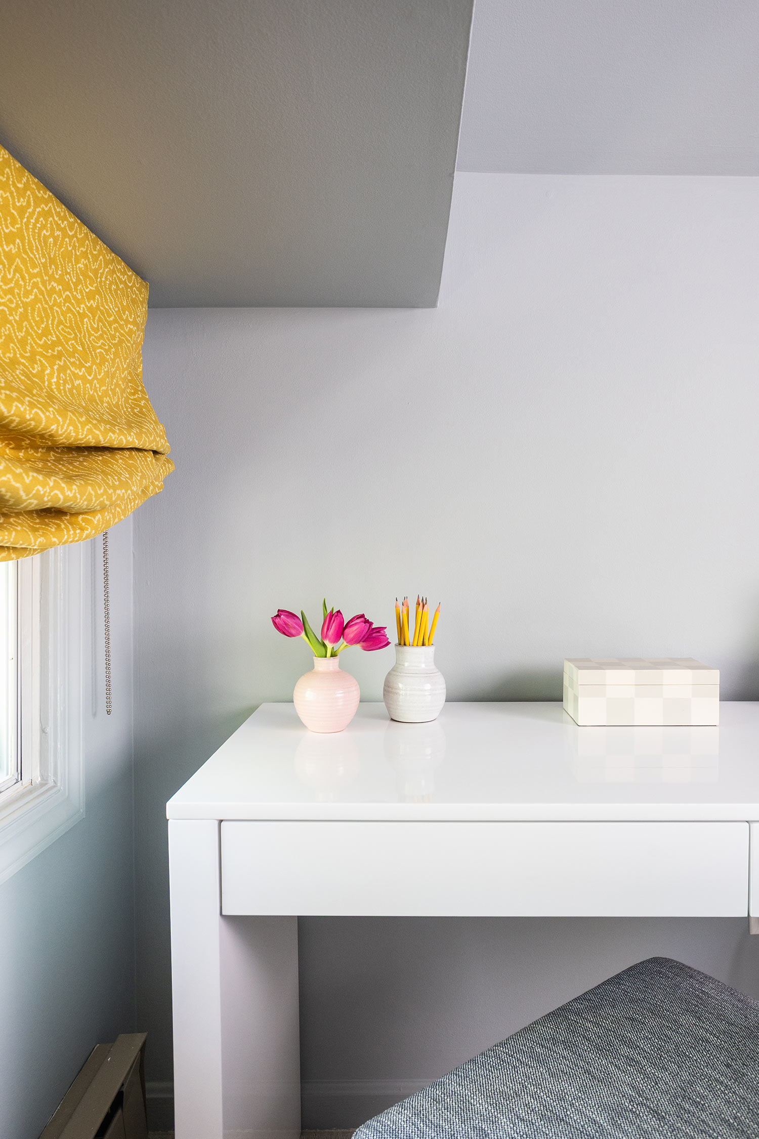 A white desk is situated against a gray wall. On the test is a small vase with pink flowers