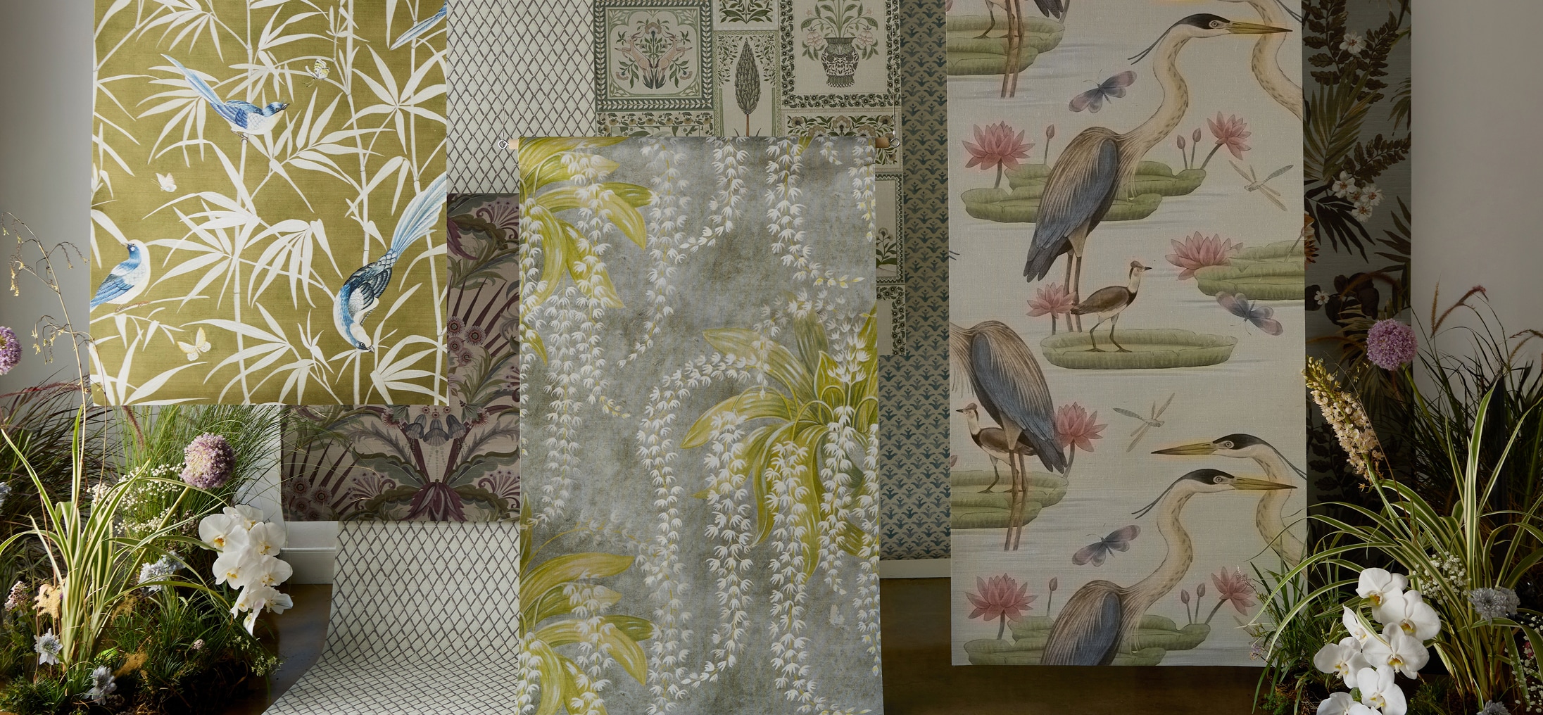 Multiple different rolls of grasscloth wallpaper hanging in a room surrounded by flowers